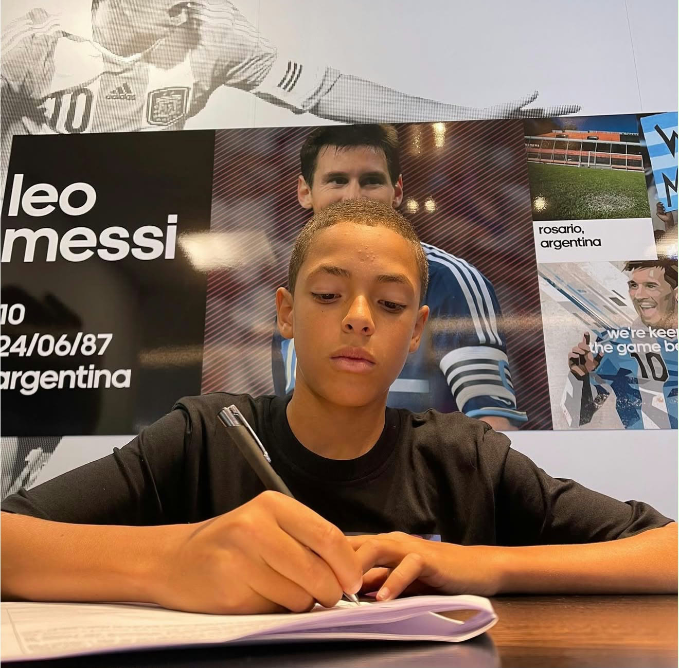 Lucas Henrique signing the contract, with a Lionel Messi panel behind him