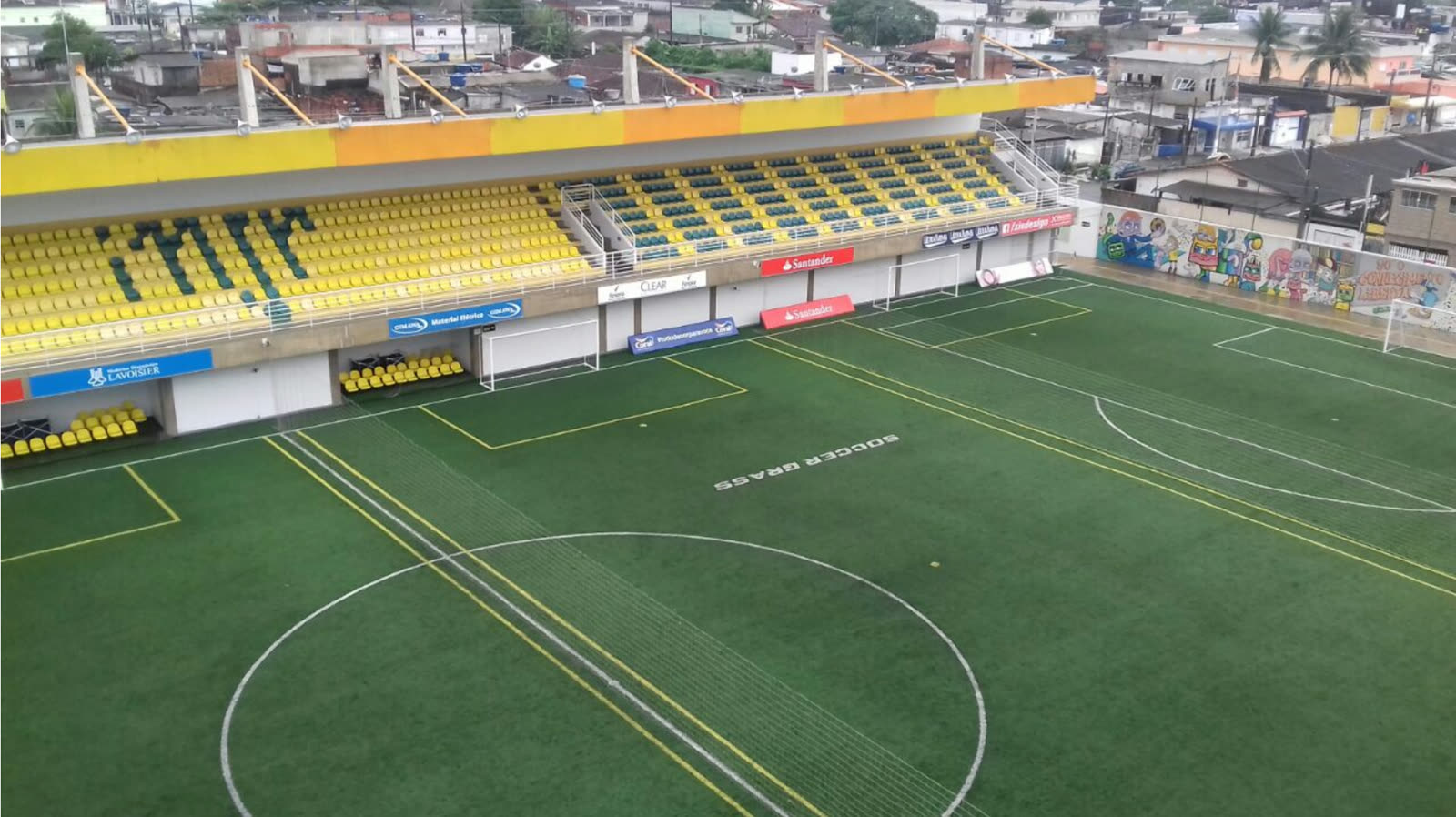 The Instituto Projeto Neymar Jr. pitch seen from the stand, with the mural and the yellow and green seats