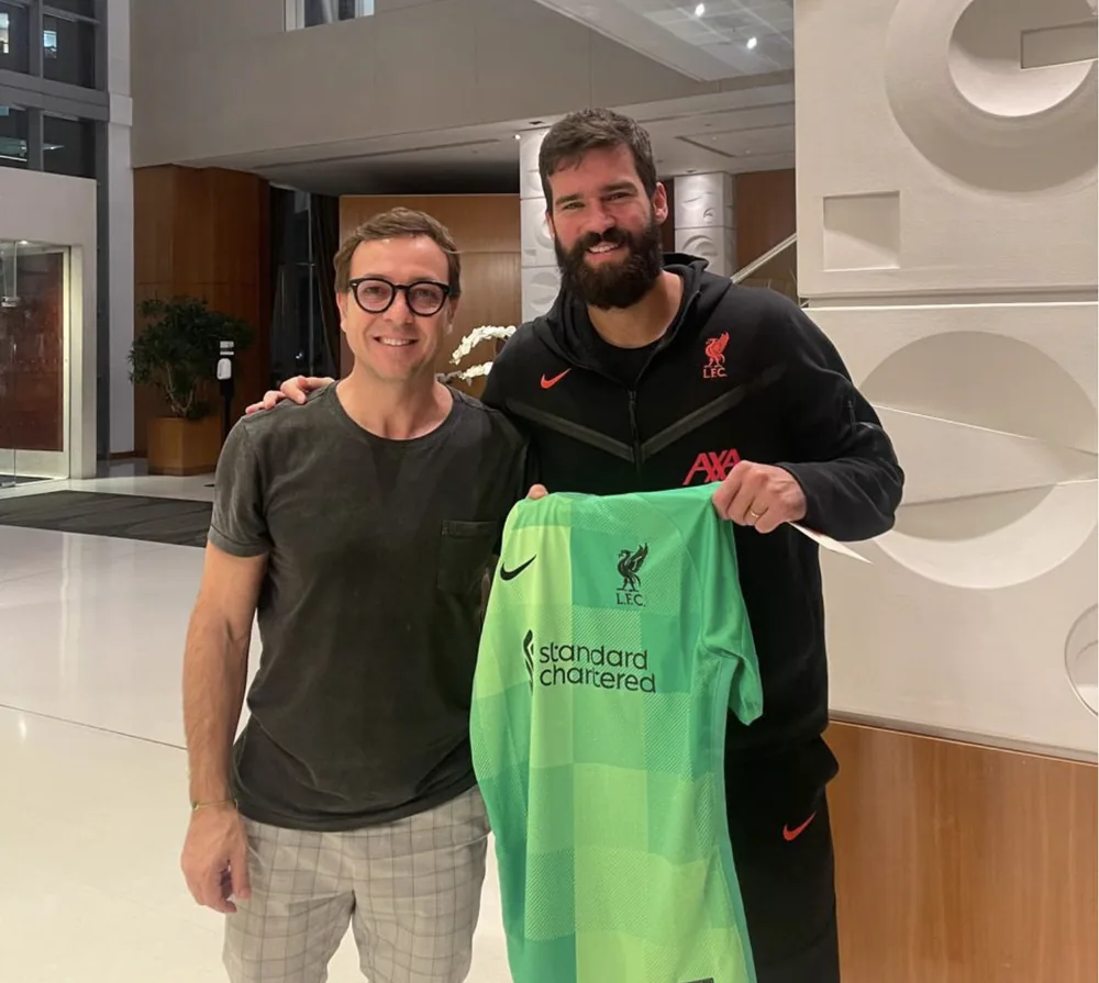 Alisson holding a Liverpool goalkeeper shirt next to Fabio Brancatelli