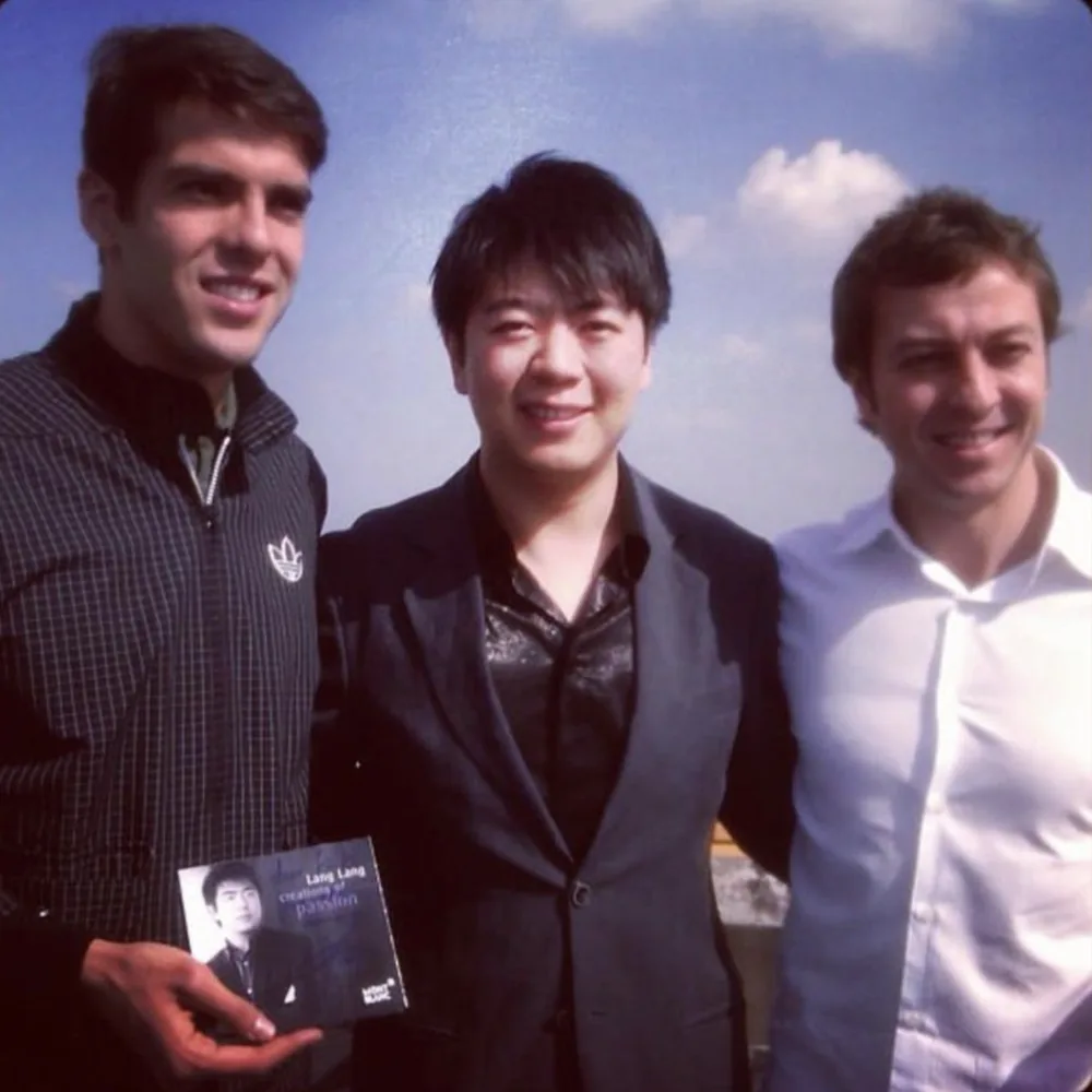 Kaká, holding a Lang Lang record, Lang Lang and Fabio Brancatelli under an open sky